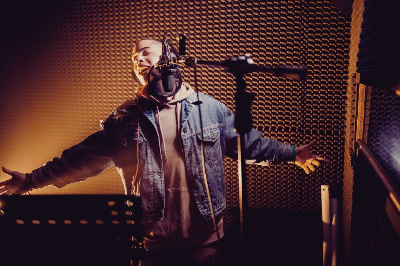 How To Get A Music Manager? An artist singing in front of a microphone in a recording studio sound booth.