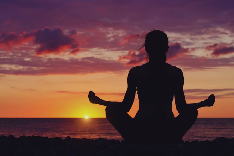 a woman sitting in a yoga pose at sunset