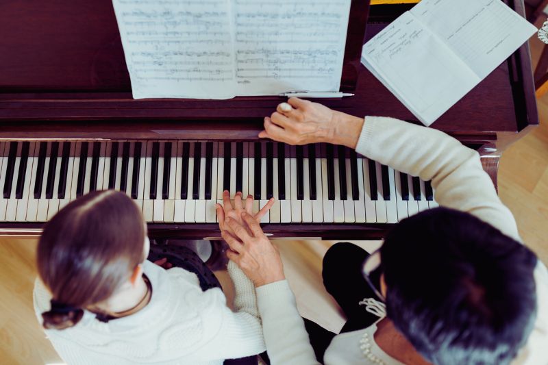 a woman teaching a girl to play piano