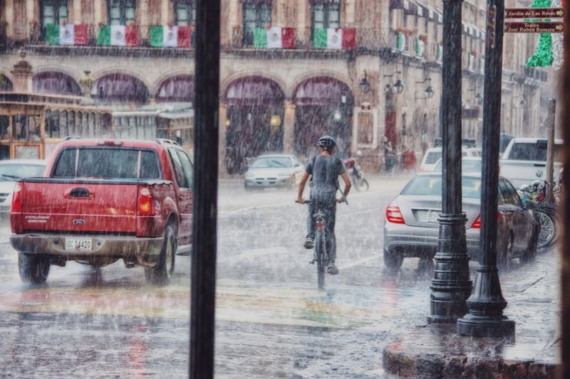 Rainy city street with cars and a man riding a bicycle