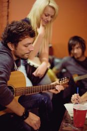 A group of musicians cowriting a song, two holding guitars and one writing down lyrics.