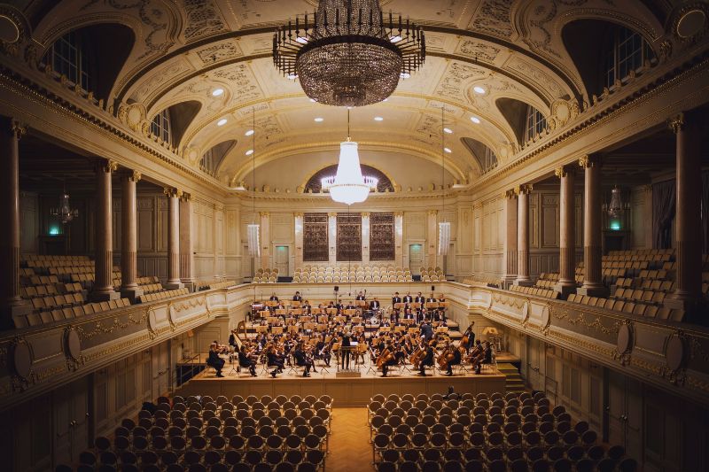 An orchestra rehearsing on the stage of a large orchestra hall.
