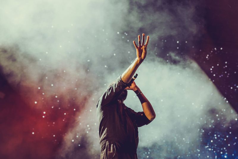 What does ep mean in music? An artist on stage singing into a microphone and pointing his hand up.