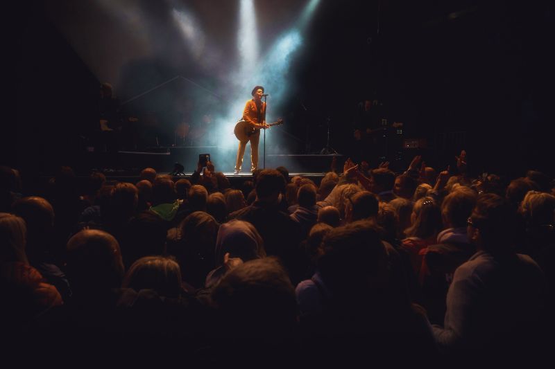 How to release music: a musical artist playing guitar on a stage with a microphone and a crowd of people in front of him.