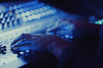 A mixing engineer's hands visible on a mixing console's faders, mixing music.