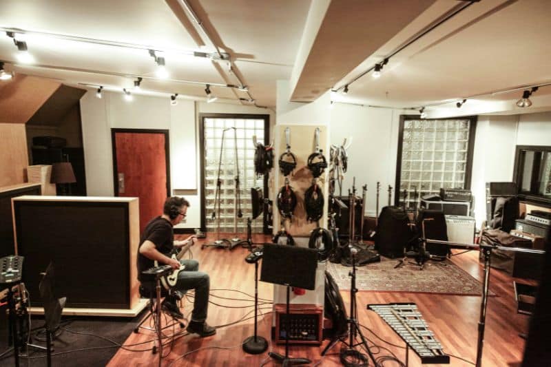 A session guitarist playing in a recording studio live room with headphones on.