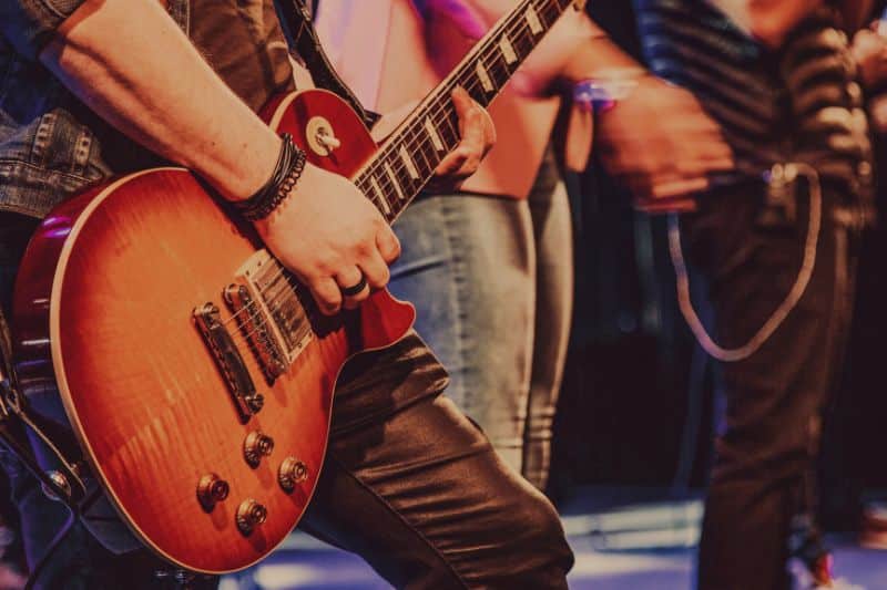 A guitarist playing a red sunburst color Les Paul guitar on stage.