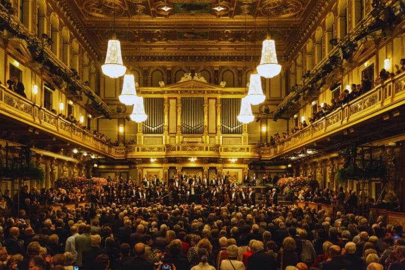 An orchestra standing on stage in fronf of a full house audience in a concert hall and end of their performance.