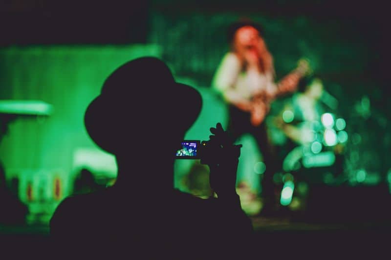 What is alternative music? A member of an audience recording a video of an alternative band's performance on the stage in front of them.