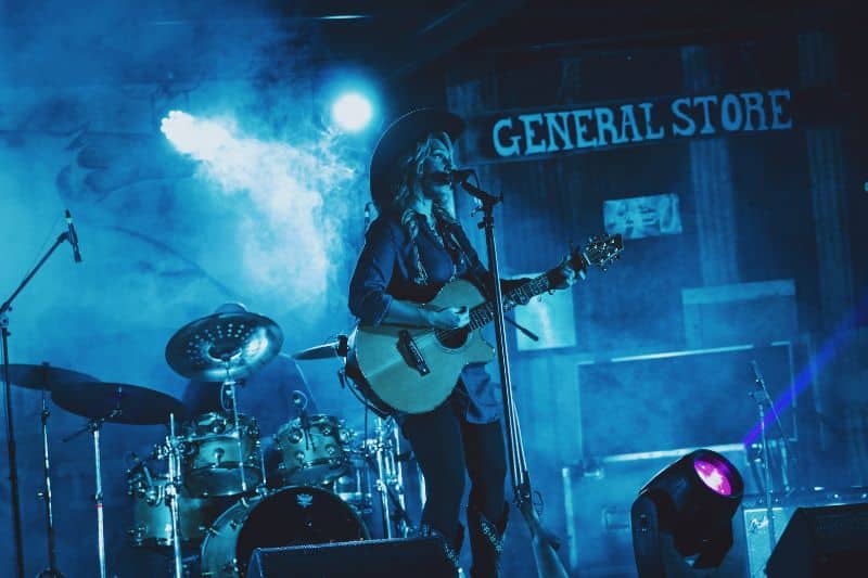 Who invented country music? A Country music artist playing guitar and singing on the stage of a club with her band.
