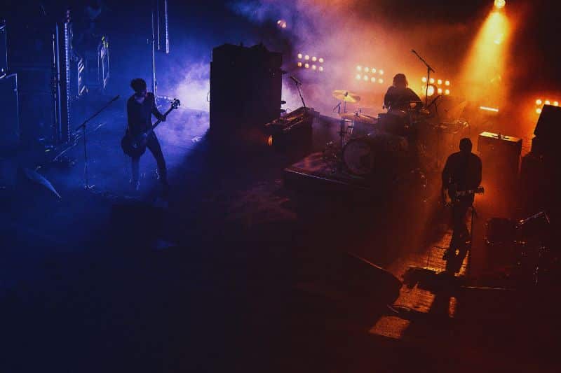 A band performing on a dark stage with colorful lights