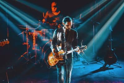 A rock band performing live on stage, with the lead singer standing at his microphone, playing his electric guitar.