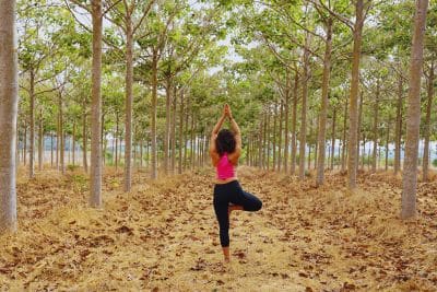 A woman practicing yoga outside in middle of the woods.
